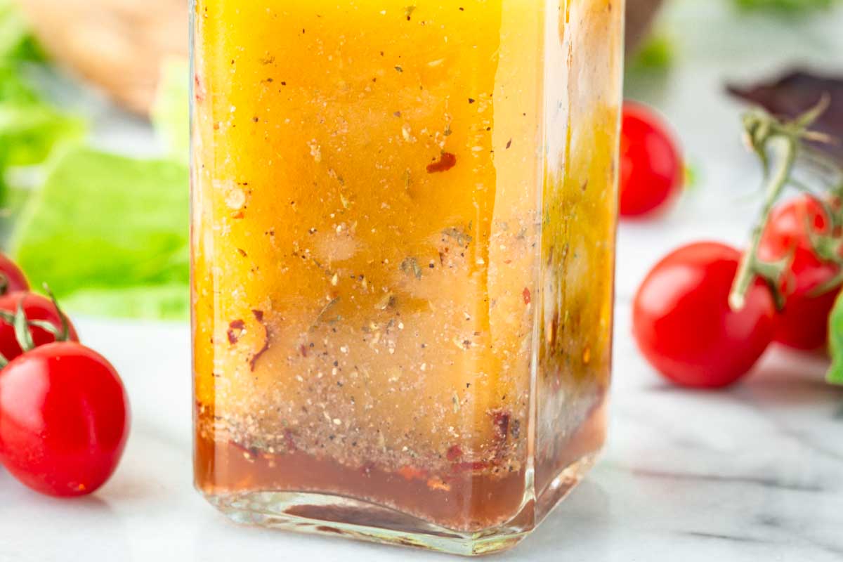 Close-up of the bottom of a glass bottle showing the separation of olive oil, vinegar, and spices in Italian dressing before shaking.
