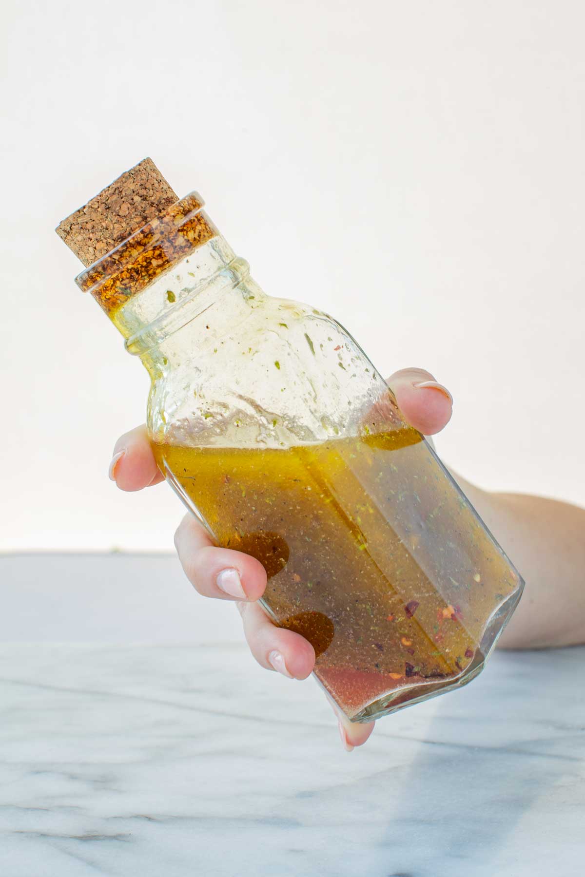 Hand holding a glass bottle of Italian dressing while giving it a quick shake to emulsify the oil, vinegar, and herbs together.