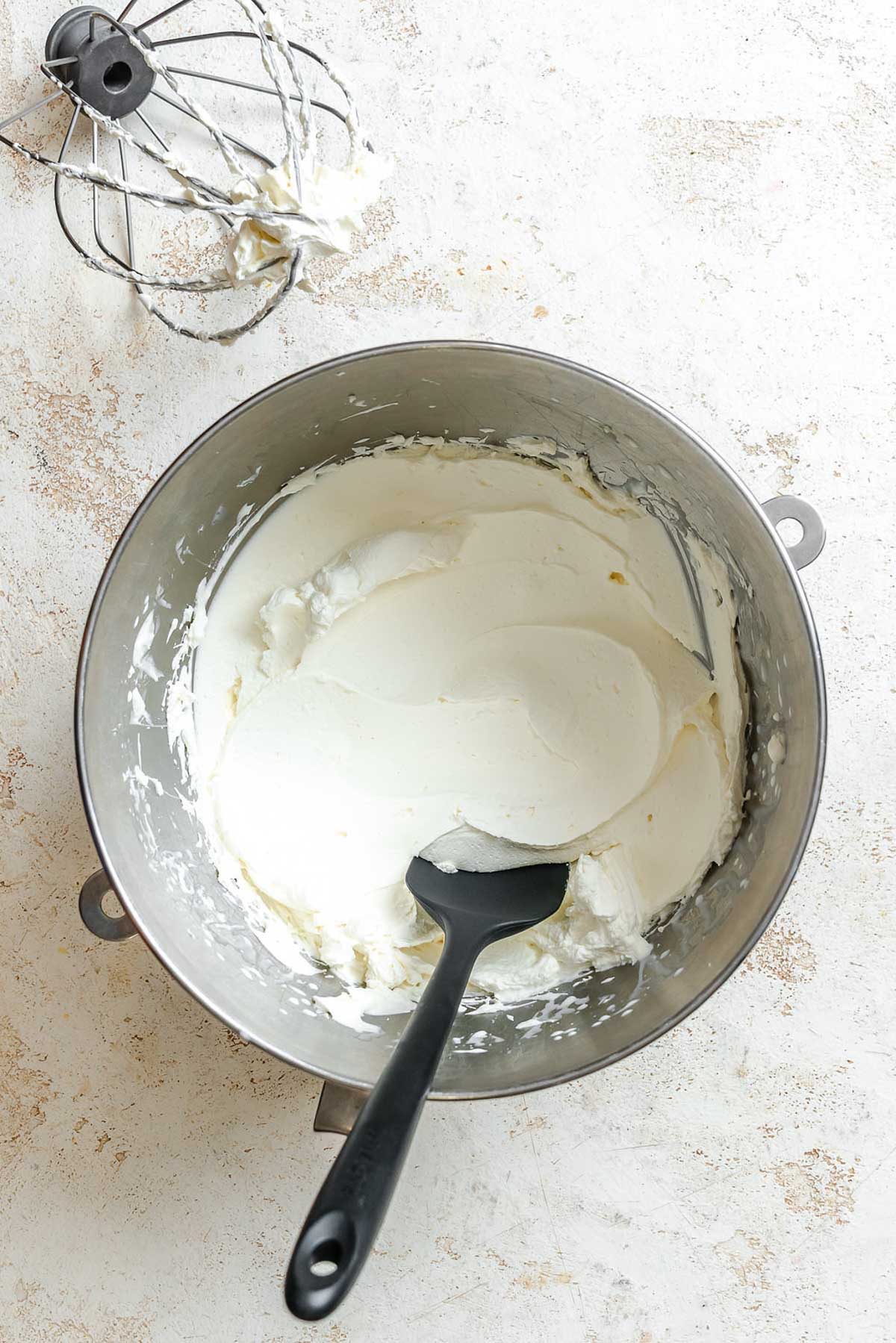 Smooth mascarpone whipped cream forming inside a mixing bowl, with a whisk attachment resting on the side.