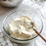 Fluffy mascarpone whipped cream scooped into a glass bowl with a spoon, showing its creamy texture and light consistency.