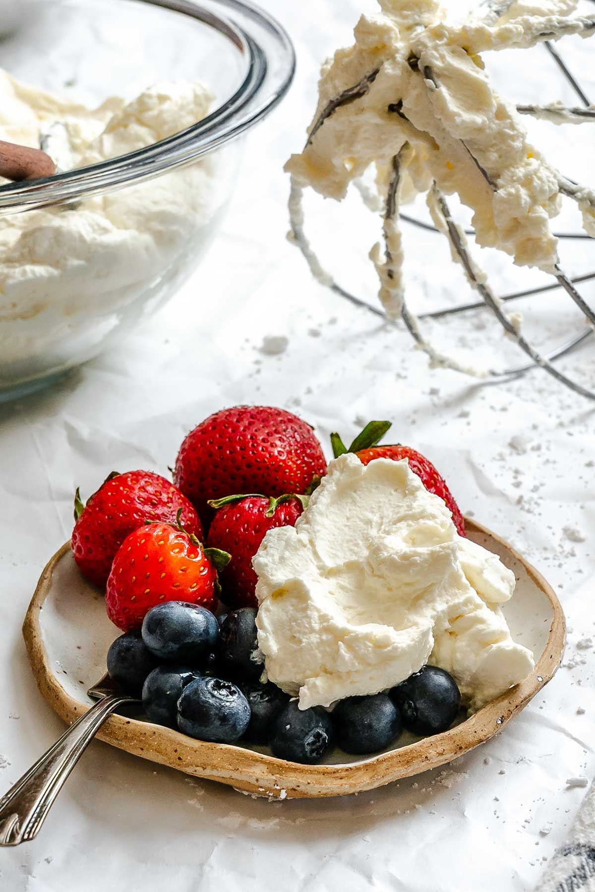 Close-up of a plate of strawberries and blueberries with a large dollop of mascarpone whipped cream, showing creamy peaks.