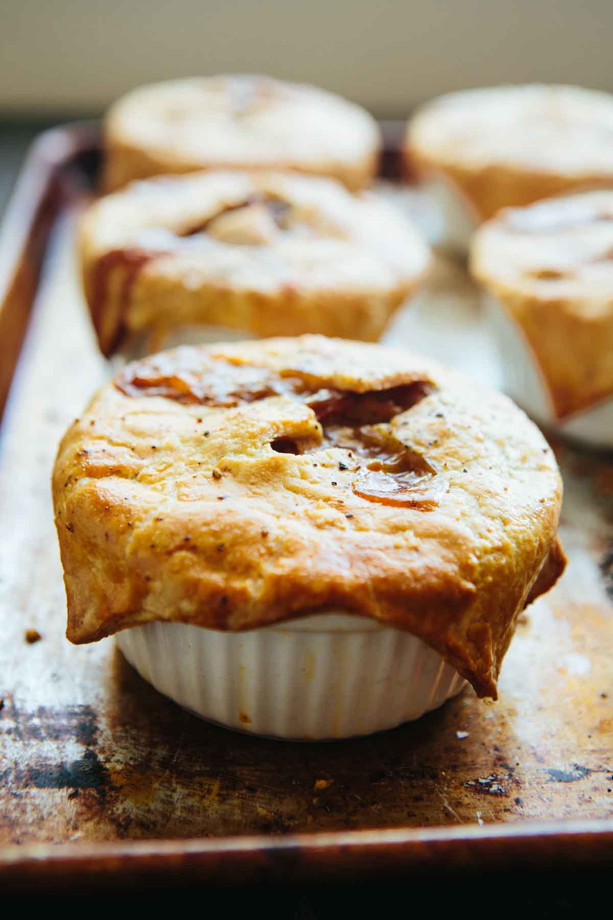 Close-up of a golden baked mini turkey pot pie in a ramekin, crust puffed and browned with juices bubbling through the top.
