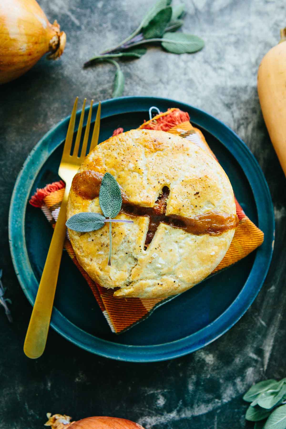Styled plate with a baked mini turkey pot pie on a teal plate, garnished with fresh sage, with a golden fork alongside.