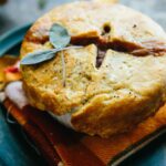 Close-up of a baked mini turkey pot pie with flaky browned crust and fresh sage garnish, served on a folded cloth napkin.