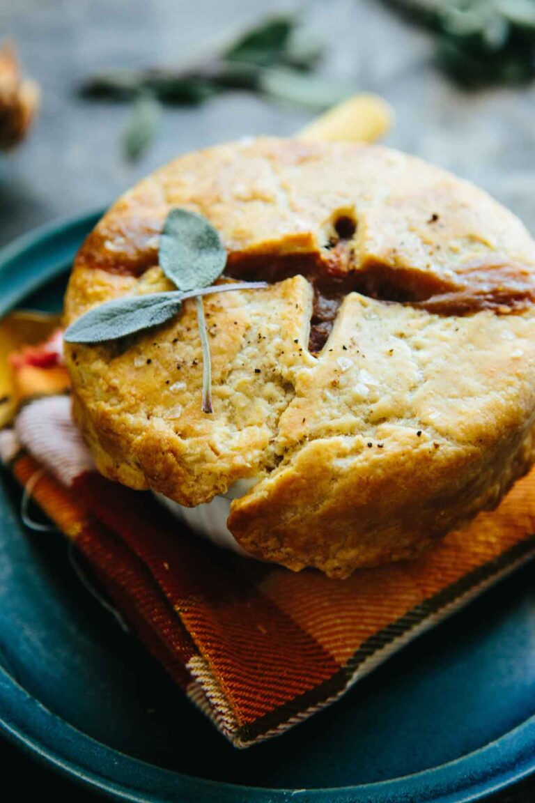 Close-up of a baked mini turkey pot pie with flaky browned crust and fresh sage garnish, served on a folded cloth napkin.