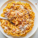A plate of pumpkin risotto topped with pancetta and grated parmesan, with a spoon tucked in.