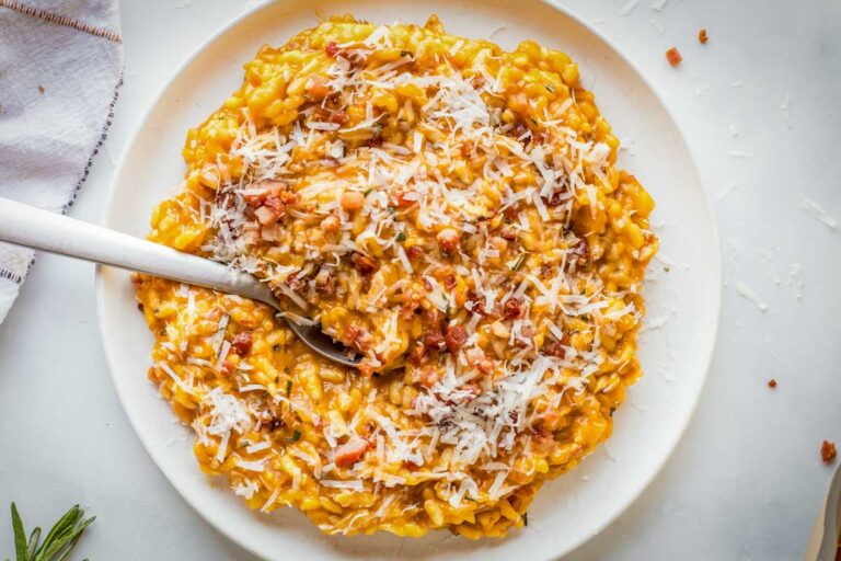 A plate of pumpkin risotto topped with pancetta and grated parmesan, with a spoon tucked in.