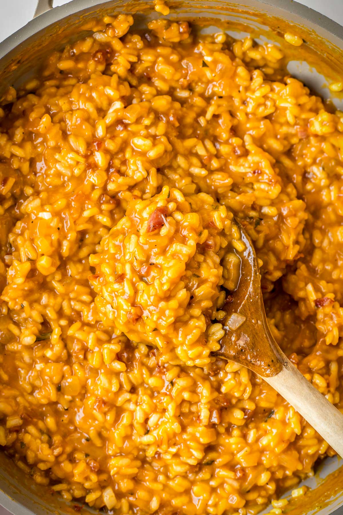 A spoonful of creamy pumpkin risotto lifted from the skillet, showing glossy texture and bits of pancetta.