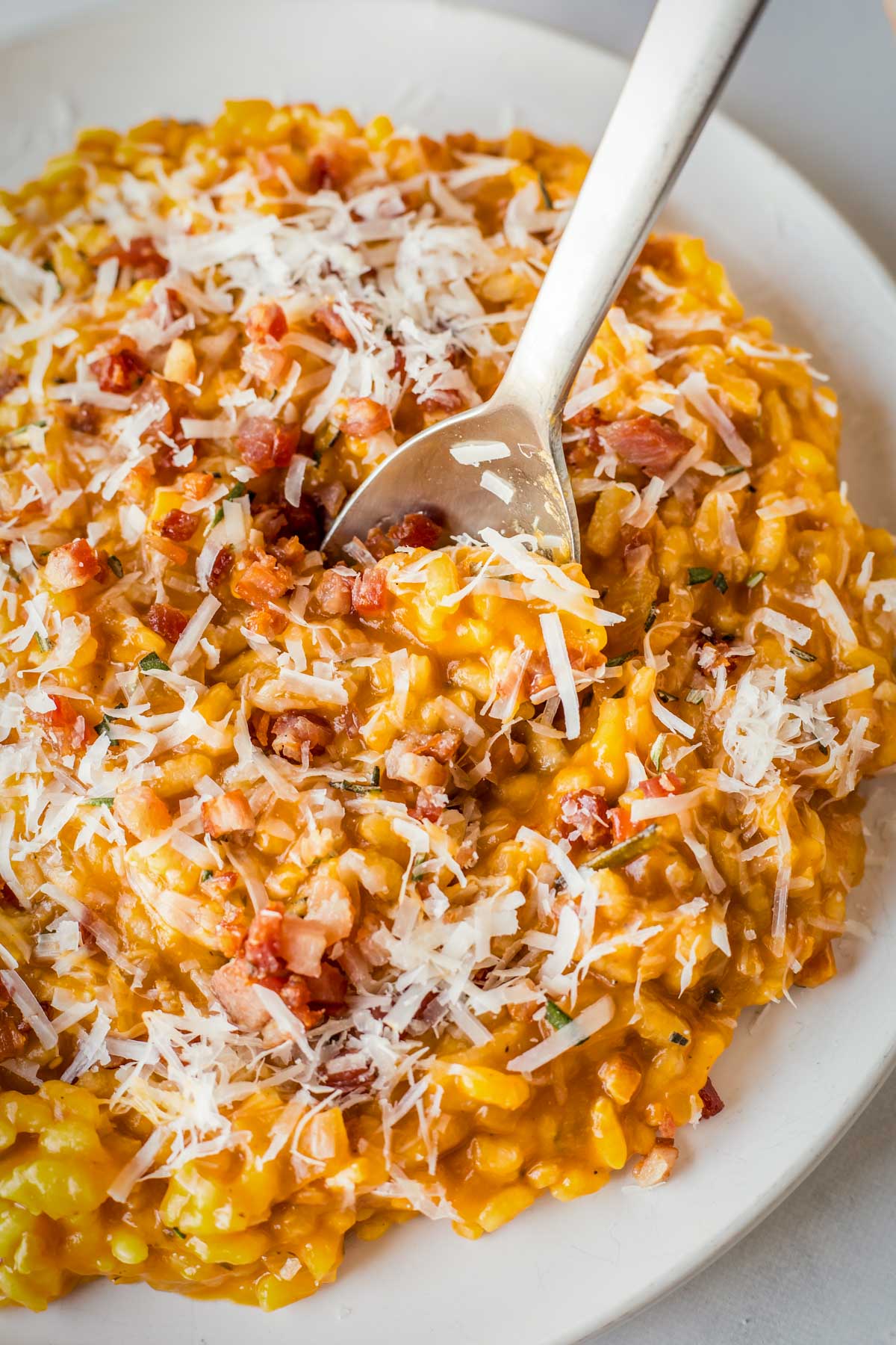 Close-up of pumpkin risotto with visible grains of rice coated in pumpkin and speckled with pancetta.