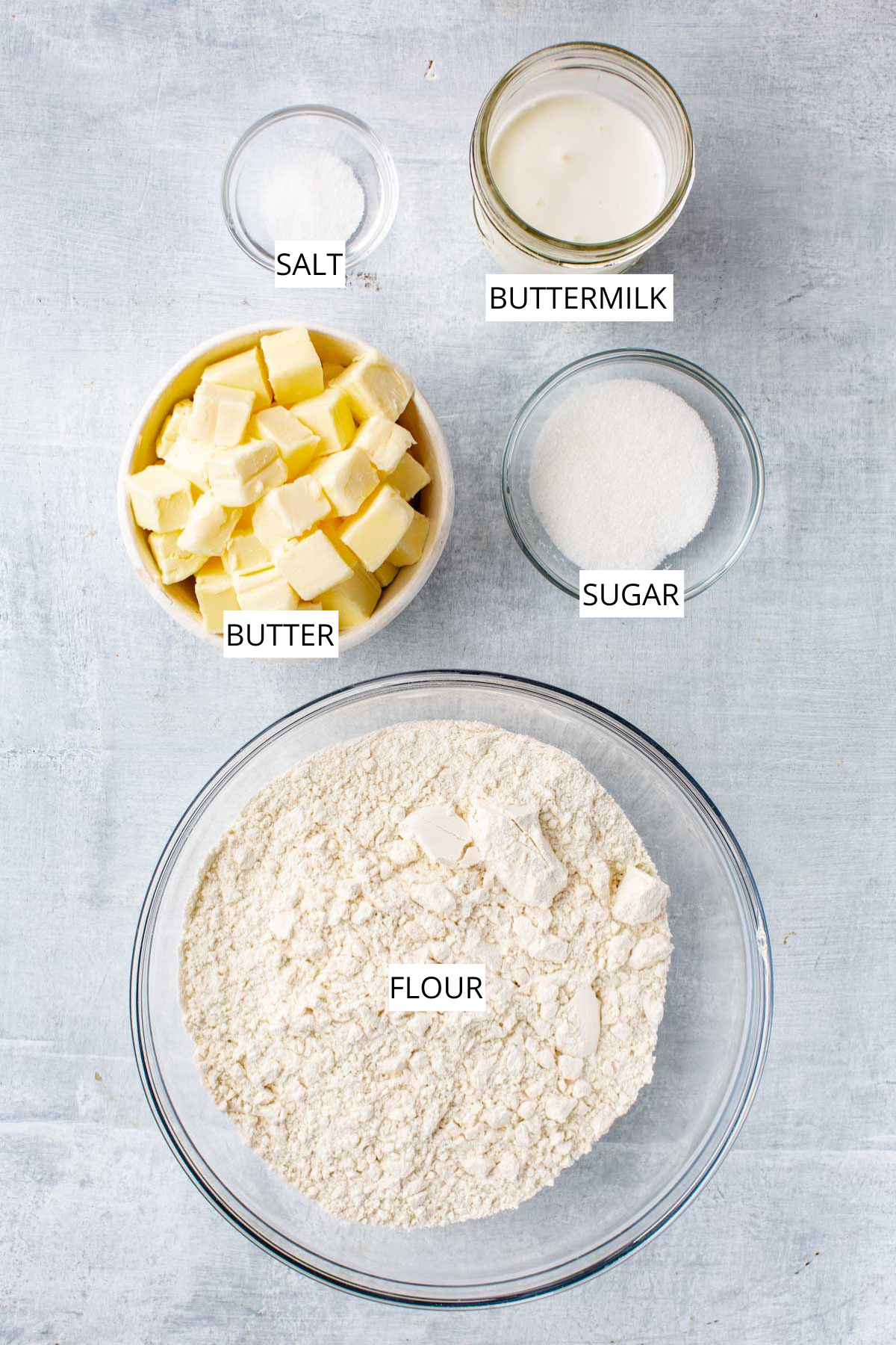 Overhead view of measured pie crust ingredients labeled as flour, butter, sugar, salt, and buttermilk.