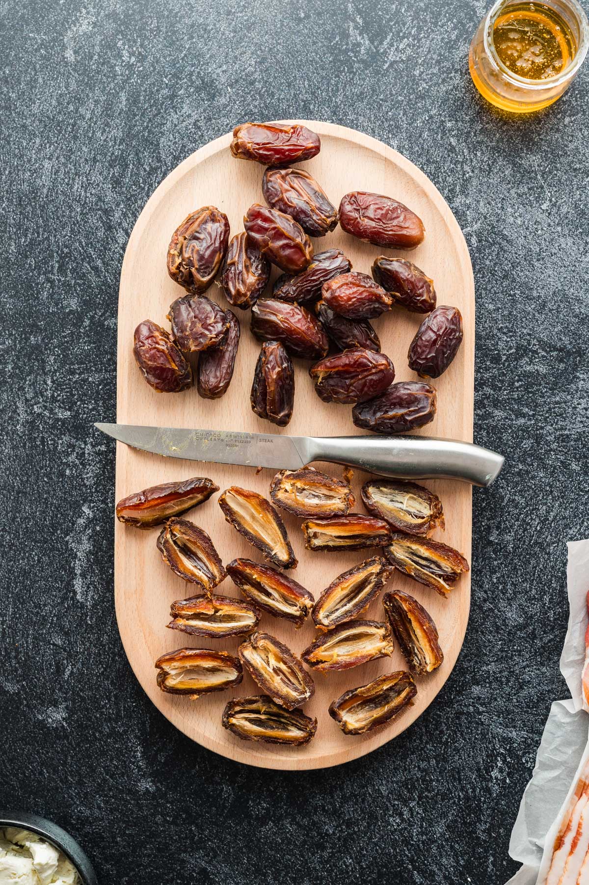 Whole and halved Medjool dates on a wooden board with a knife, ready for pitting and stuffing.