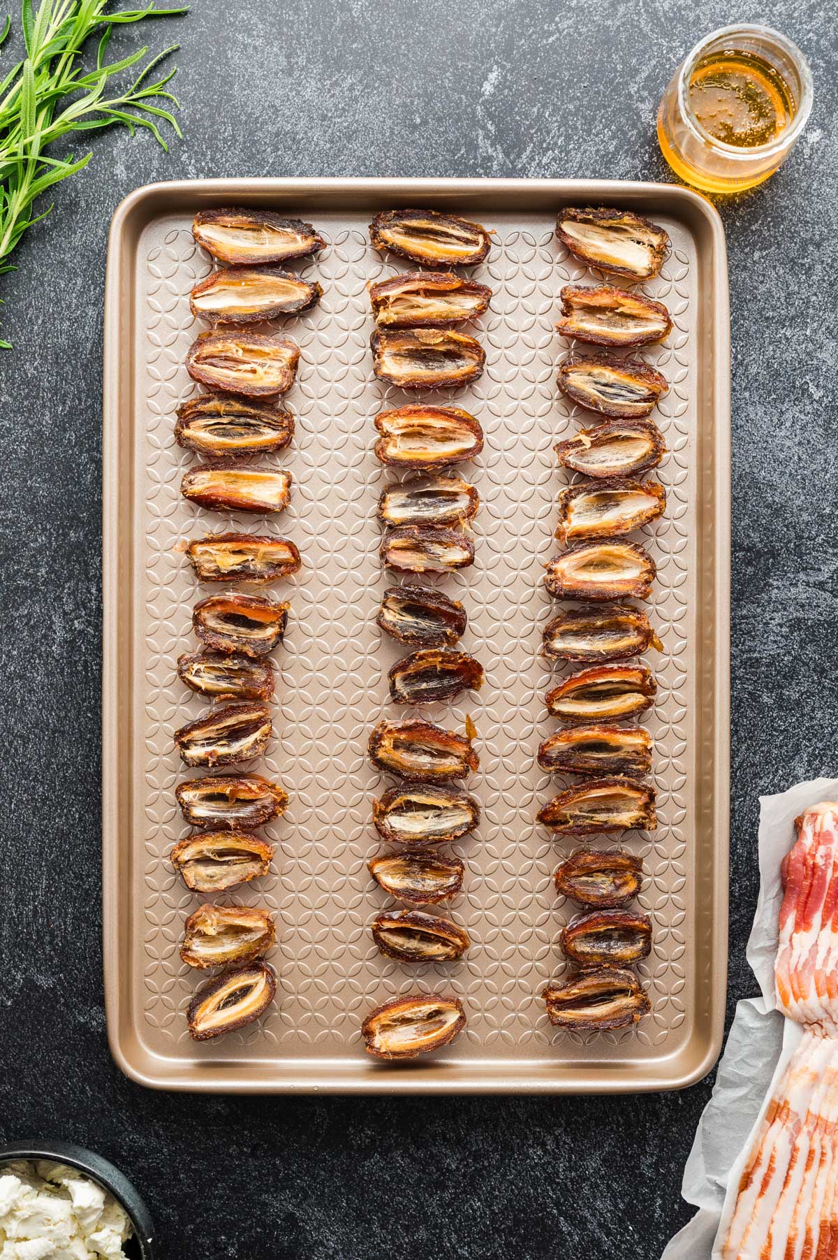 Halved dates arranged on a baking sheet, ready to be filled with cheese.