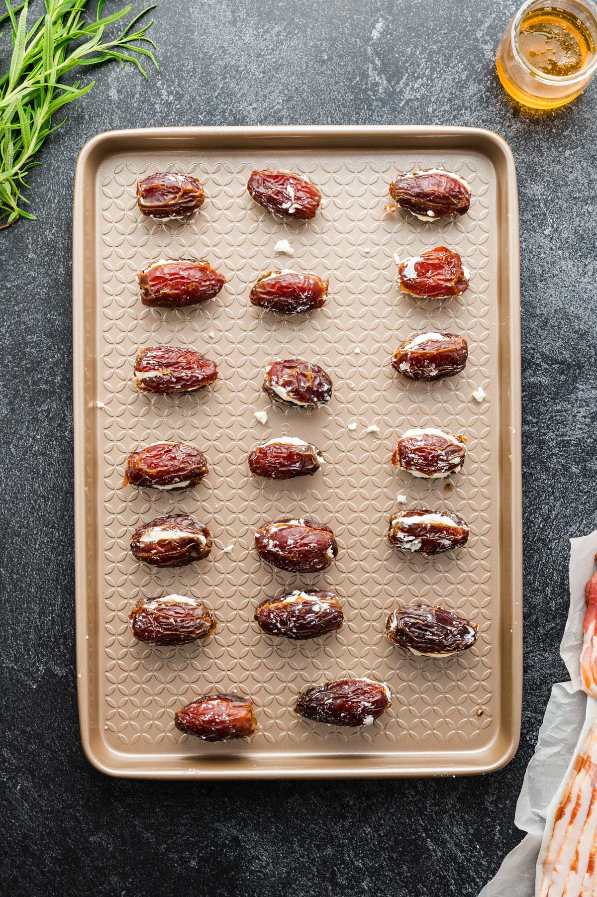 Stuffed dates pressed back together on a baking sheet, prepped for wrapping.