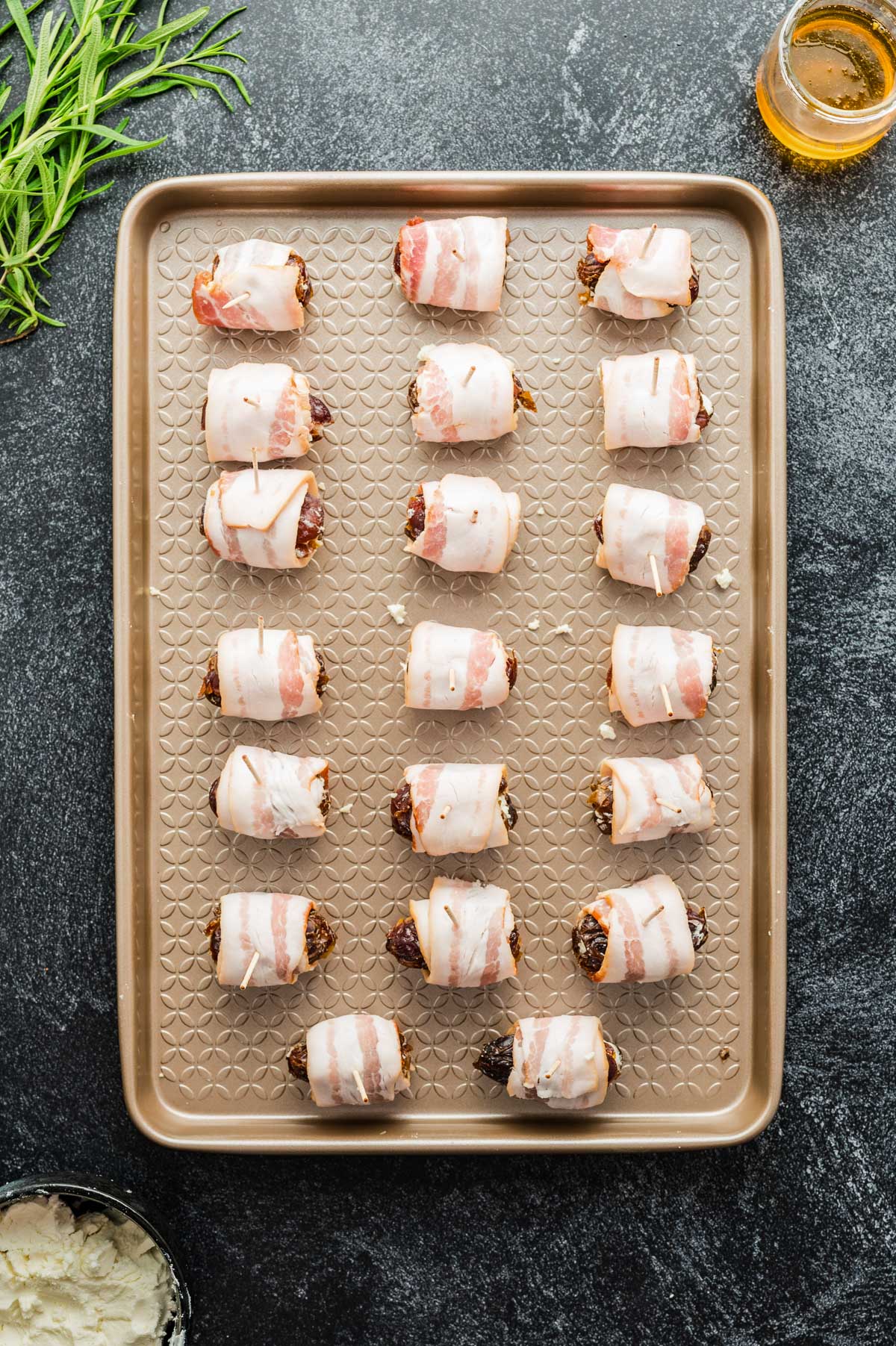 Dates wrapped in bacon and secured with toothpicks on a baking sheet before baking.