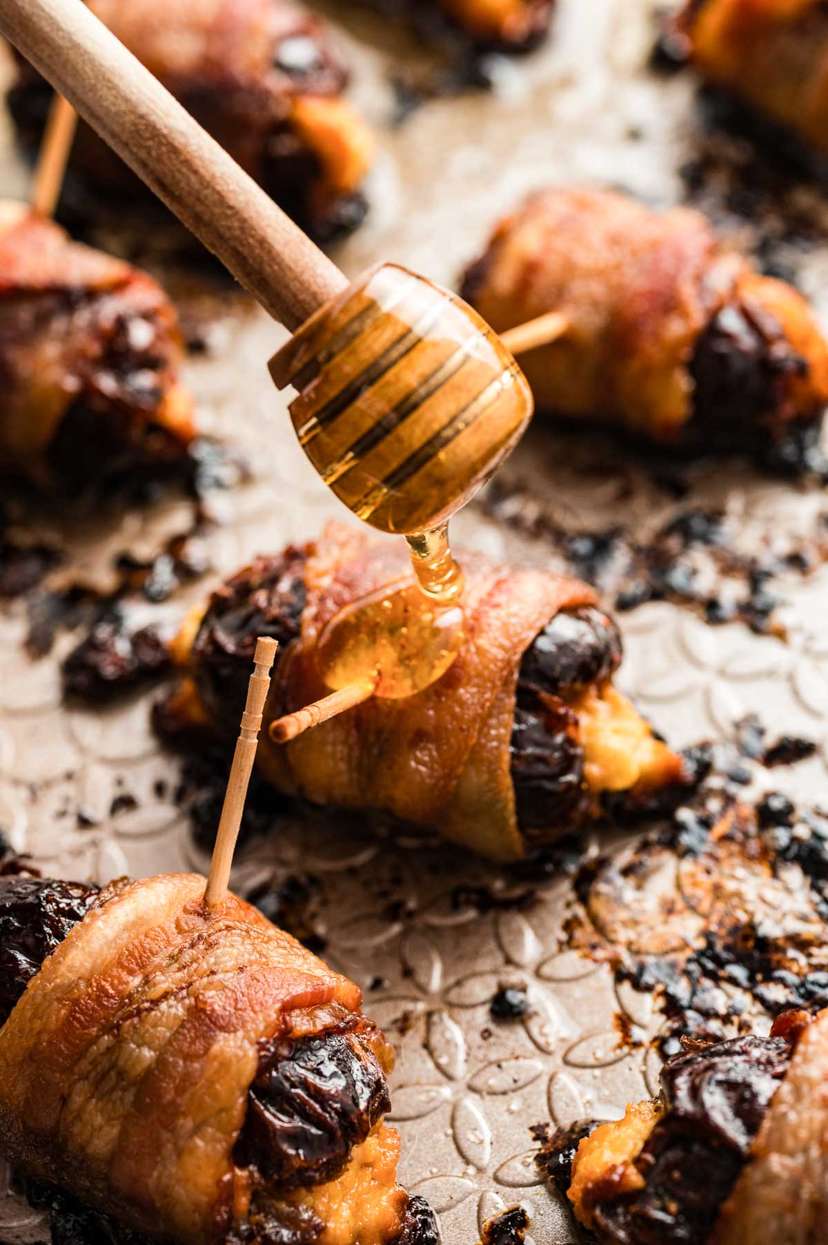 Honey being drizzled over freshly baked bacon-wrapped dates on the sheet pan.