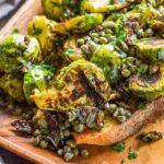 Close-up of crispy Brussels sprouts and briny capers on toasted bread, coated in glossy lemon-anchovy butter sauce.
