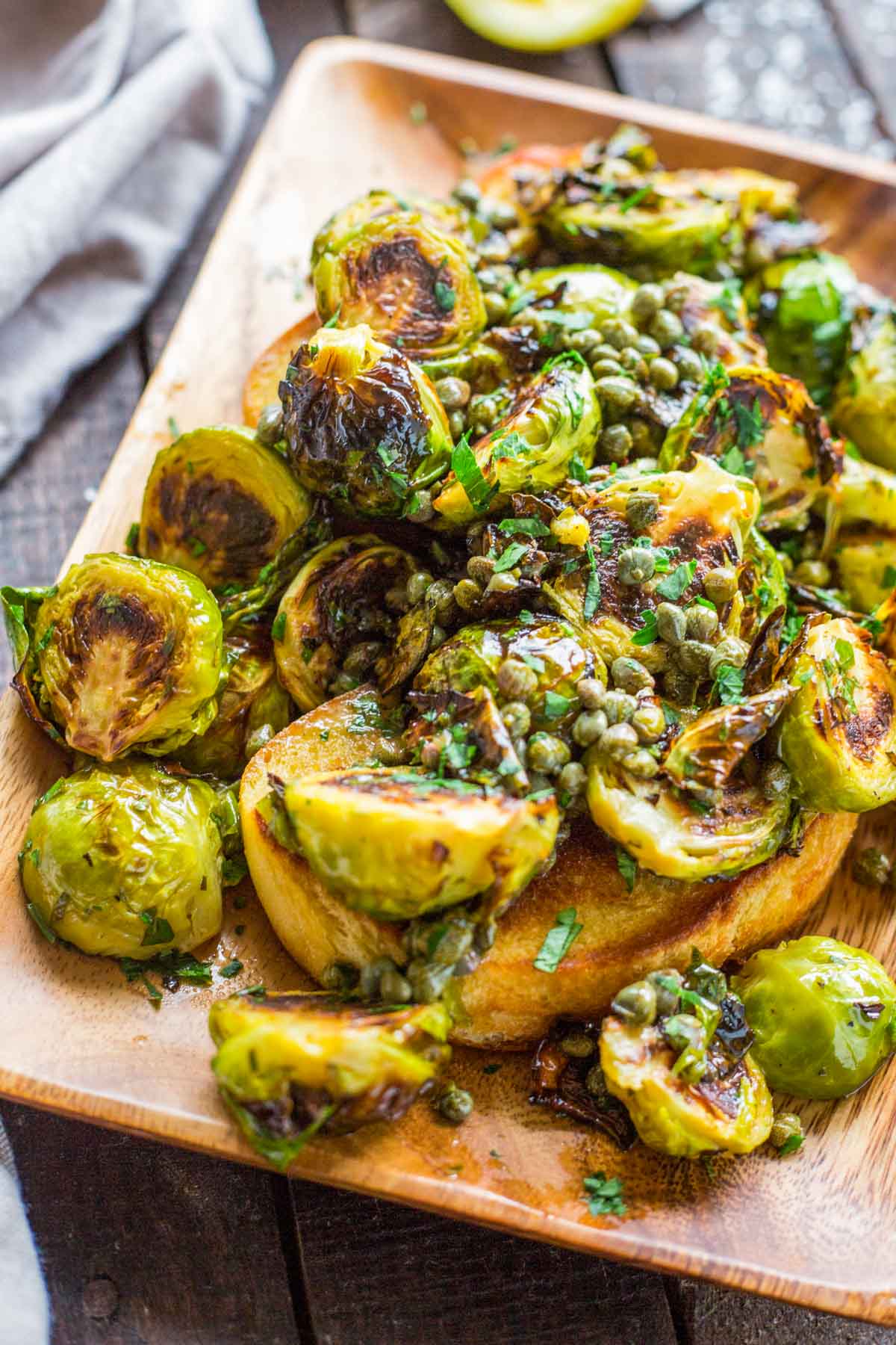 Overhead view of caramelized Brussels sprouts and capers piled over toasted bread, finished with melted butter and chopped parsley.