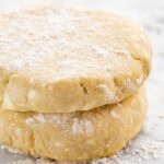 Two floured discs of pie dough stacked on top of each other, showing a buttery texture and flaky layers.