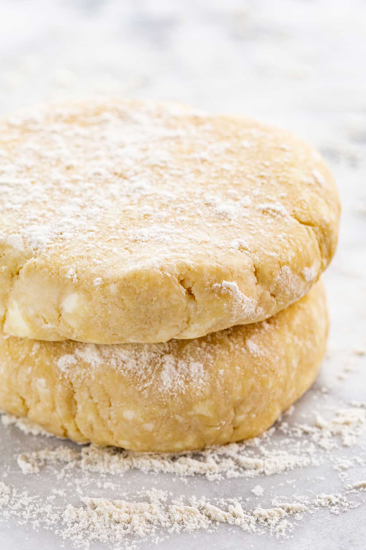 Two floured discs of pie dough stacked on top of each other, showing a buttery texture and flaky layers.