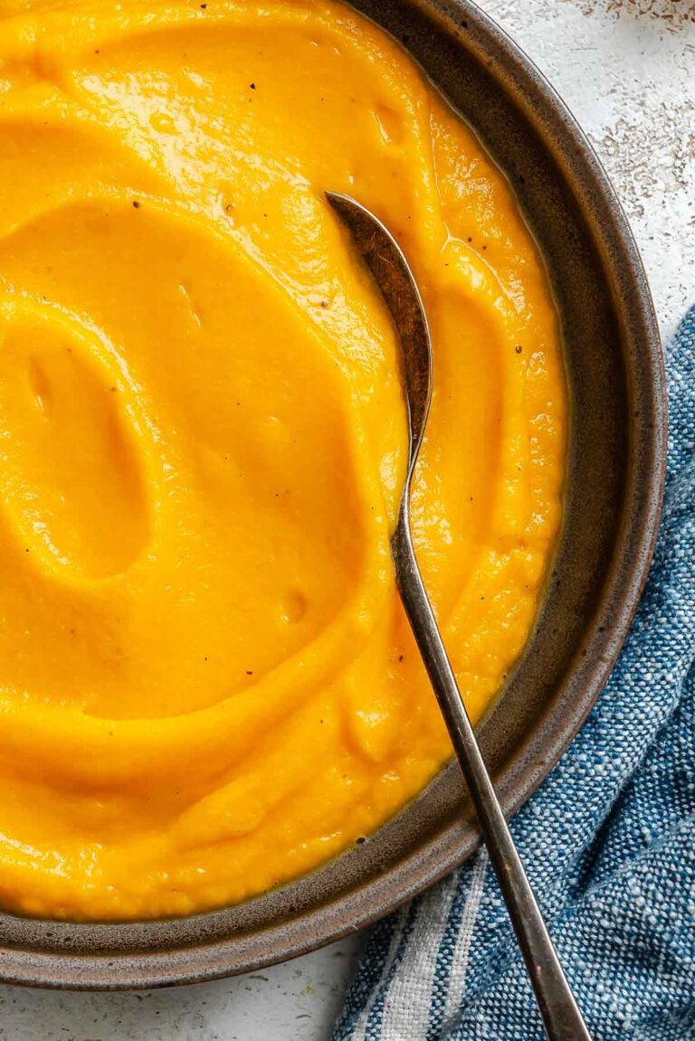 Close-up of smooth, creamy butternut squash puree in a dark bowl with a spoon resting inside.