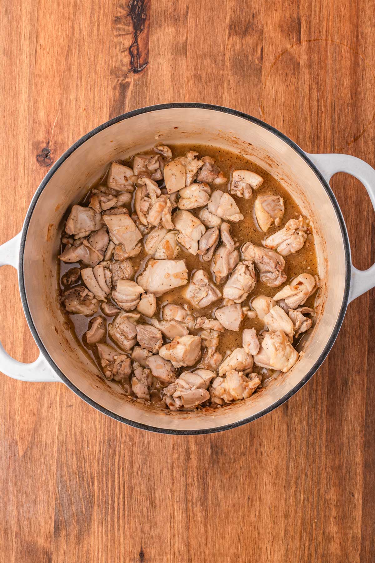 Chicken thighs simmering in a Dutch oven after being browned, beginning to form the base of the soup.