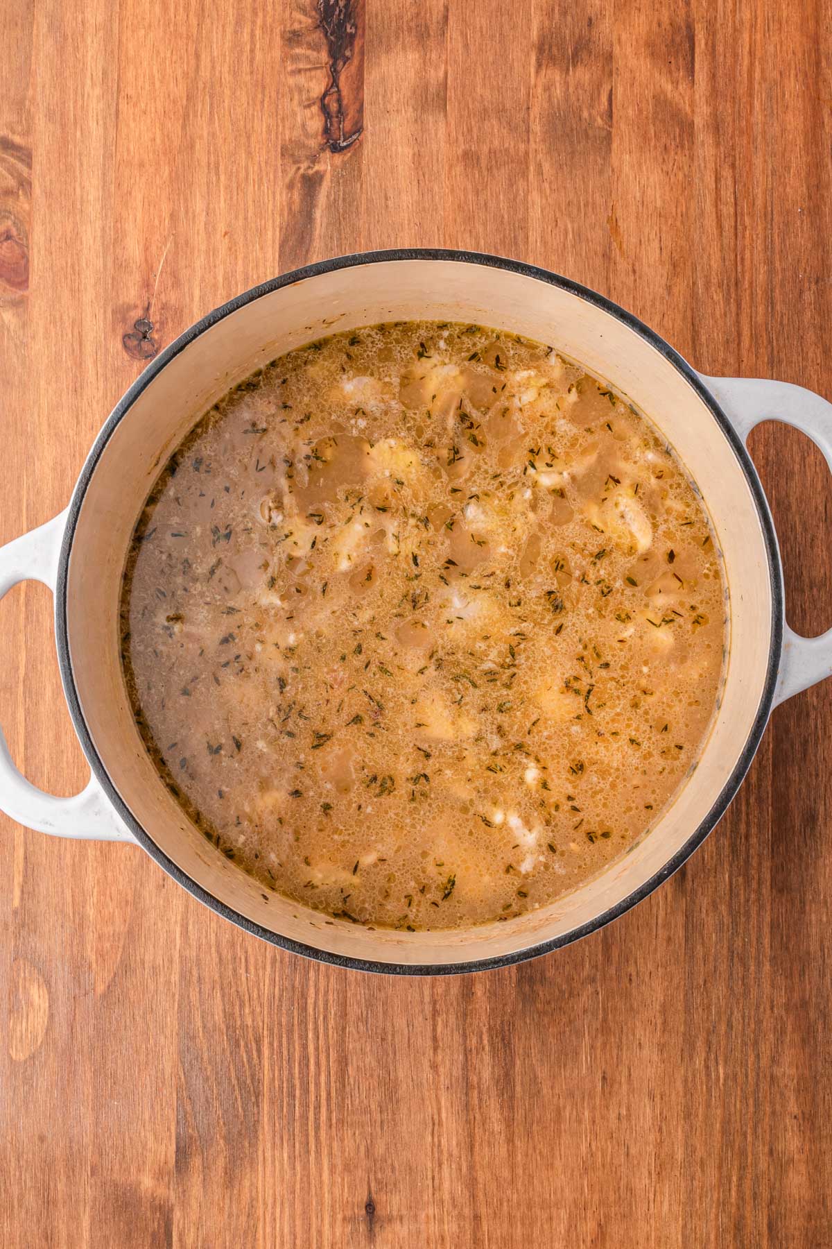 Chicken simmering in broth with thyme in a Dutch oven for chicken Florentine soup.