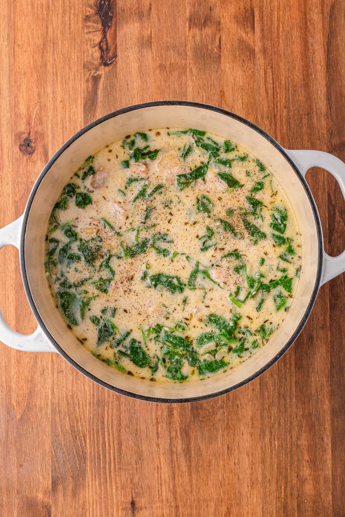 Fresh spinach added to creamy chicken soup in a Dutch oven, just beginning to wilt.