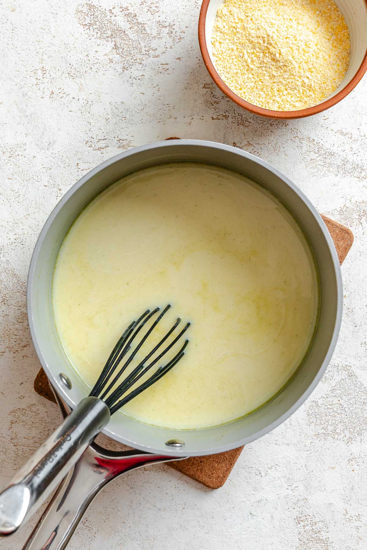 Saucepan of hot stock and milk being whisked together before adding cornmeal to start cooking polenta.