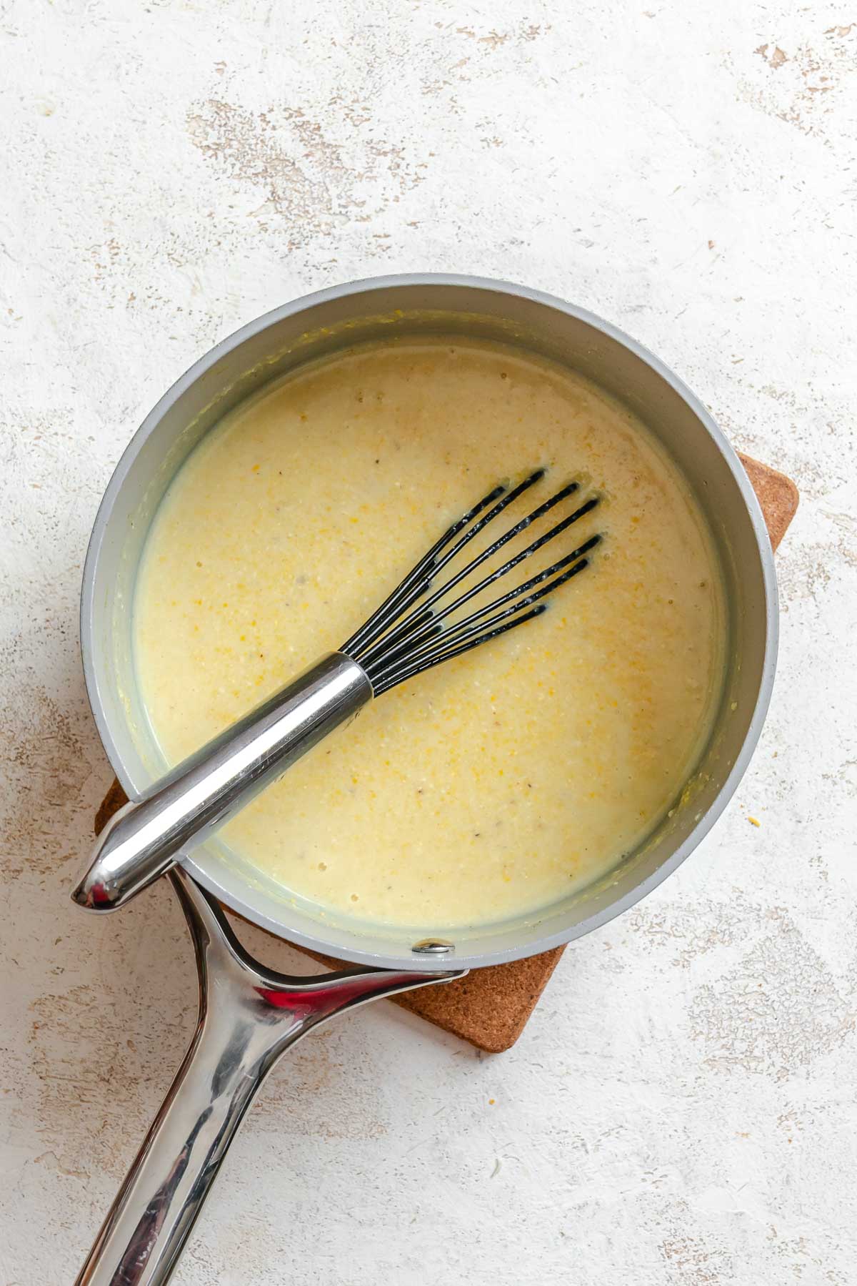Polenta beginning to thicken in the saucepan, with a whisk resting inside.