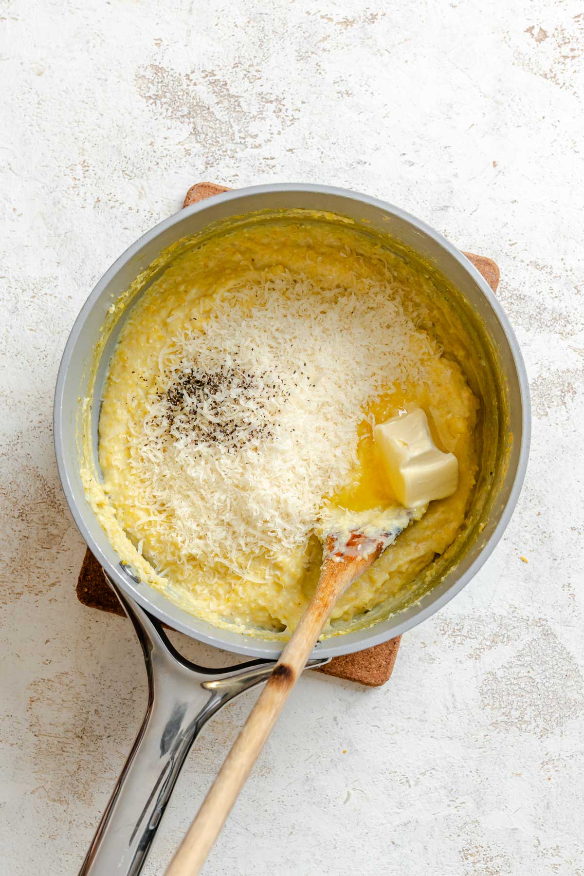 Partially cooked polenta with grated parmesan, butter, and black pepper added on top, ready to stir in.