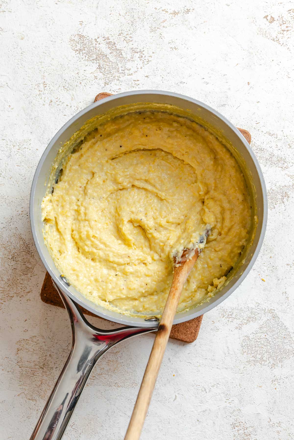Thickened, creamy polenta in a saucepan being stirred with a wooden spoon.