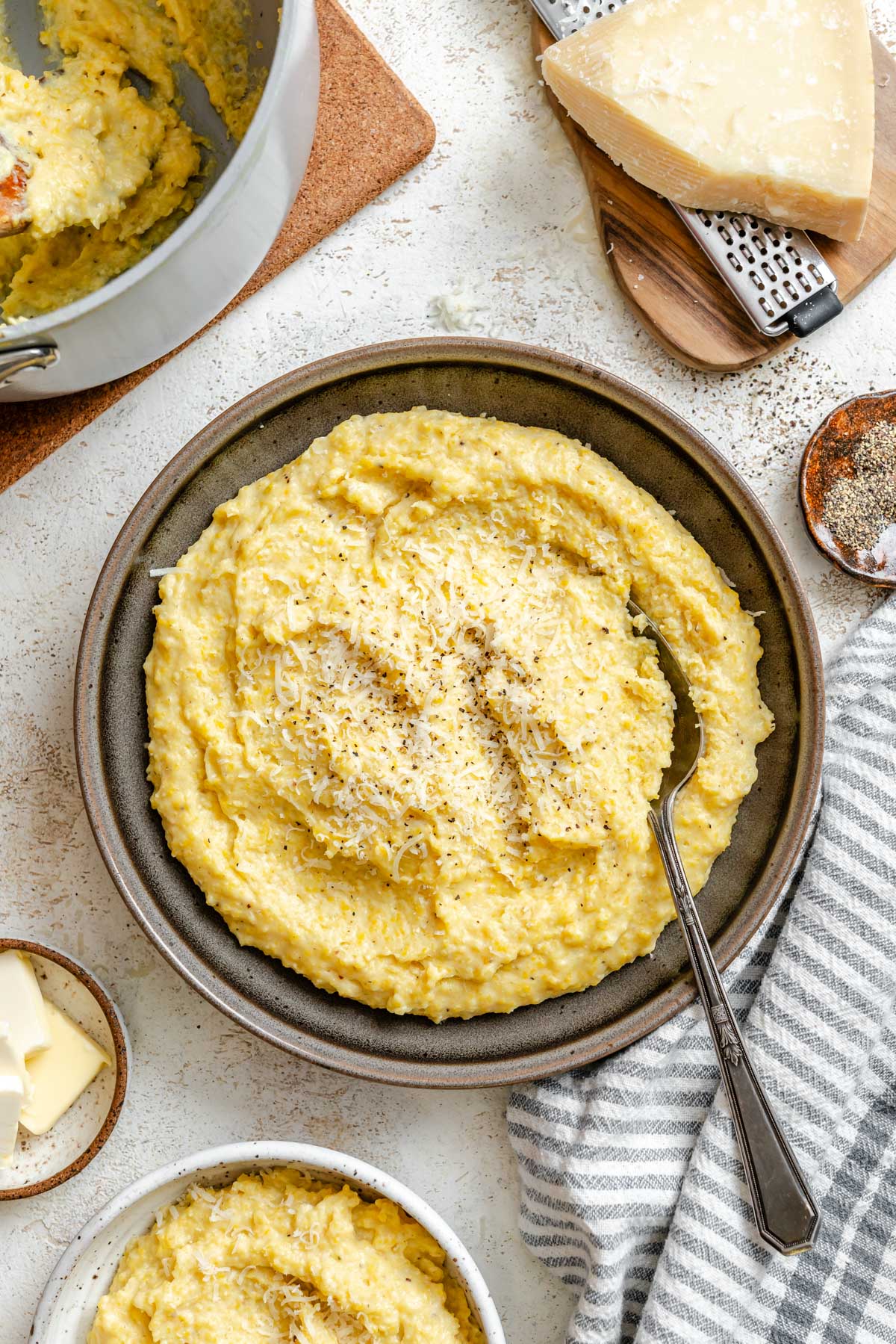 Finished creamy parmesan polenta in a serving bowl, topped with grated cheese and cracked pepper.