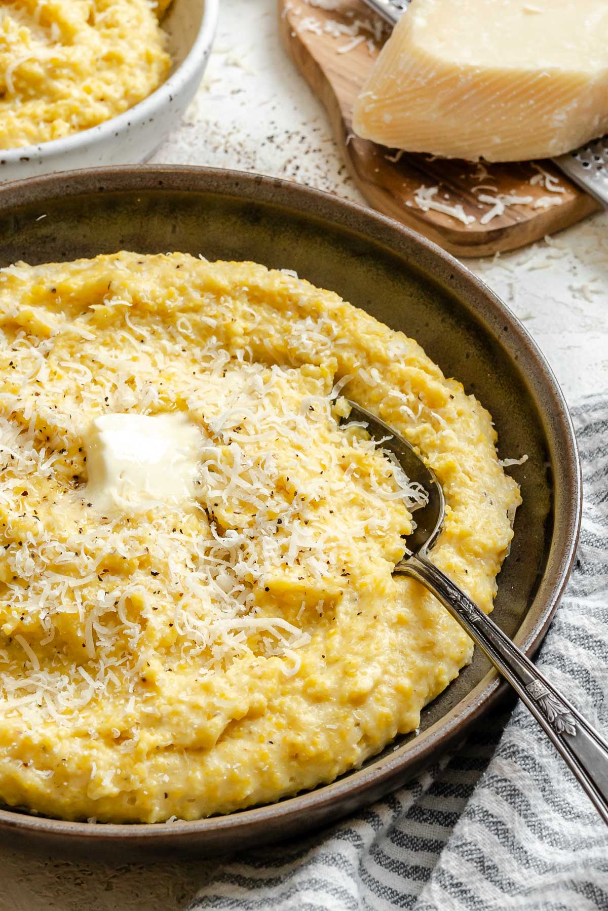 Overhead view of creamy parmesan polenta in a rustic bowl beside parmesan cheese and butter.