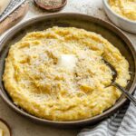 Wide photo of a bowl of parmesan polenta topped with butter and freshly grated cheese, ready to serve.