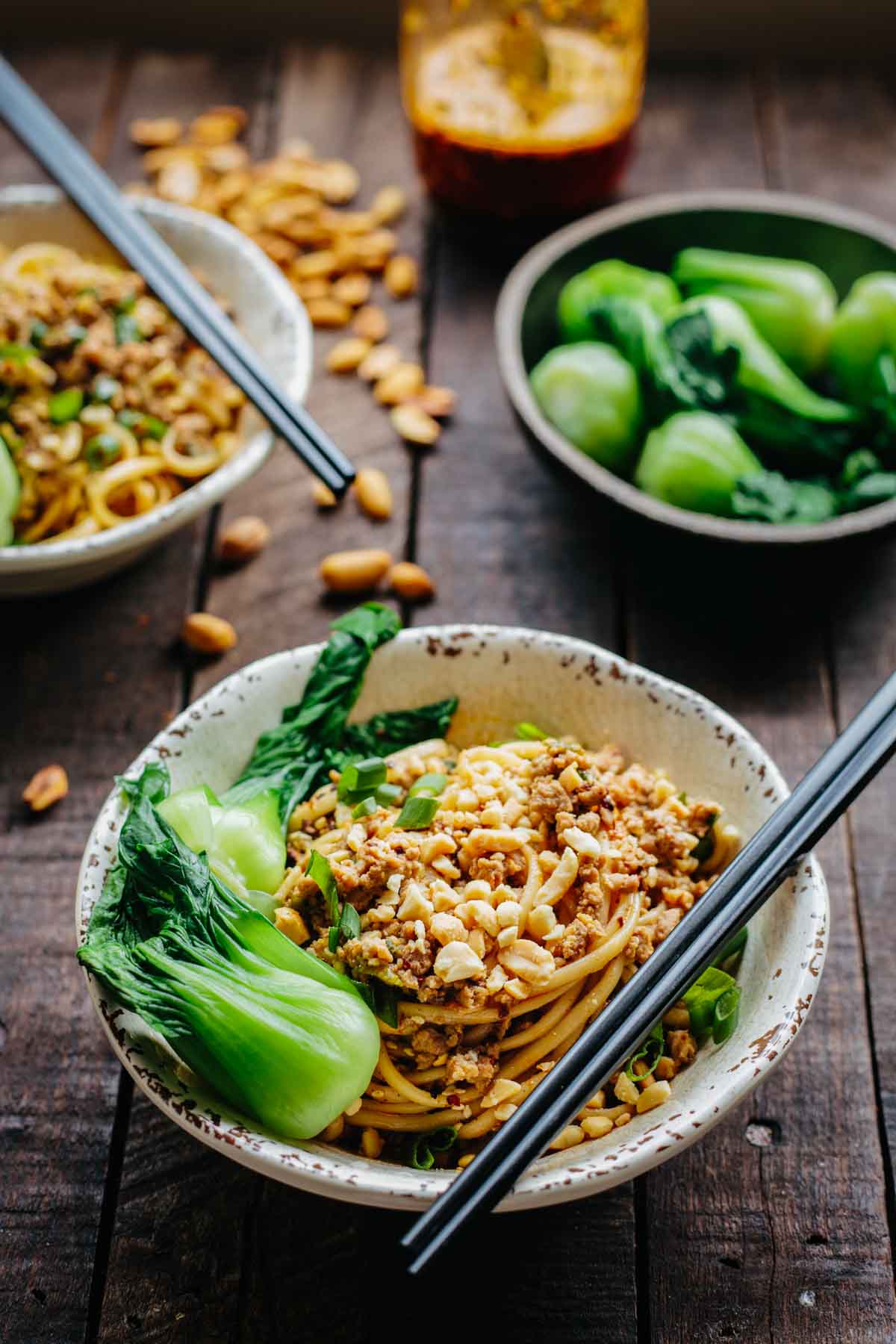 Overhead view of Dan Dan noodles garnished with green onions, bok choy, and chopped peanuts.