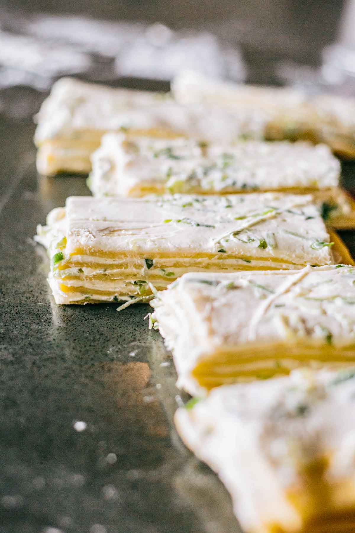 Close-up of dough strips layered with scallion cream cheese, ready to be stacked.