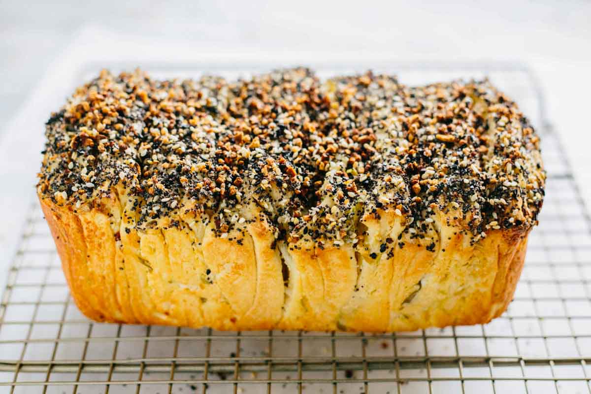 Baked loaf covered in everything bagel seasoning, cooling on a wire rack.