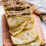 Sliced loaf on a wooden board showing tender, layered interior with scallion cream cheese.