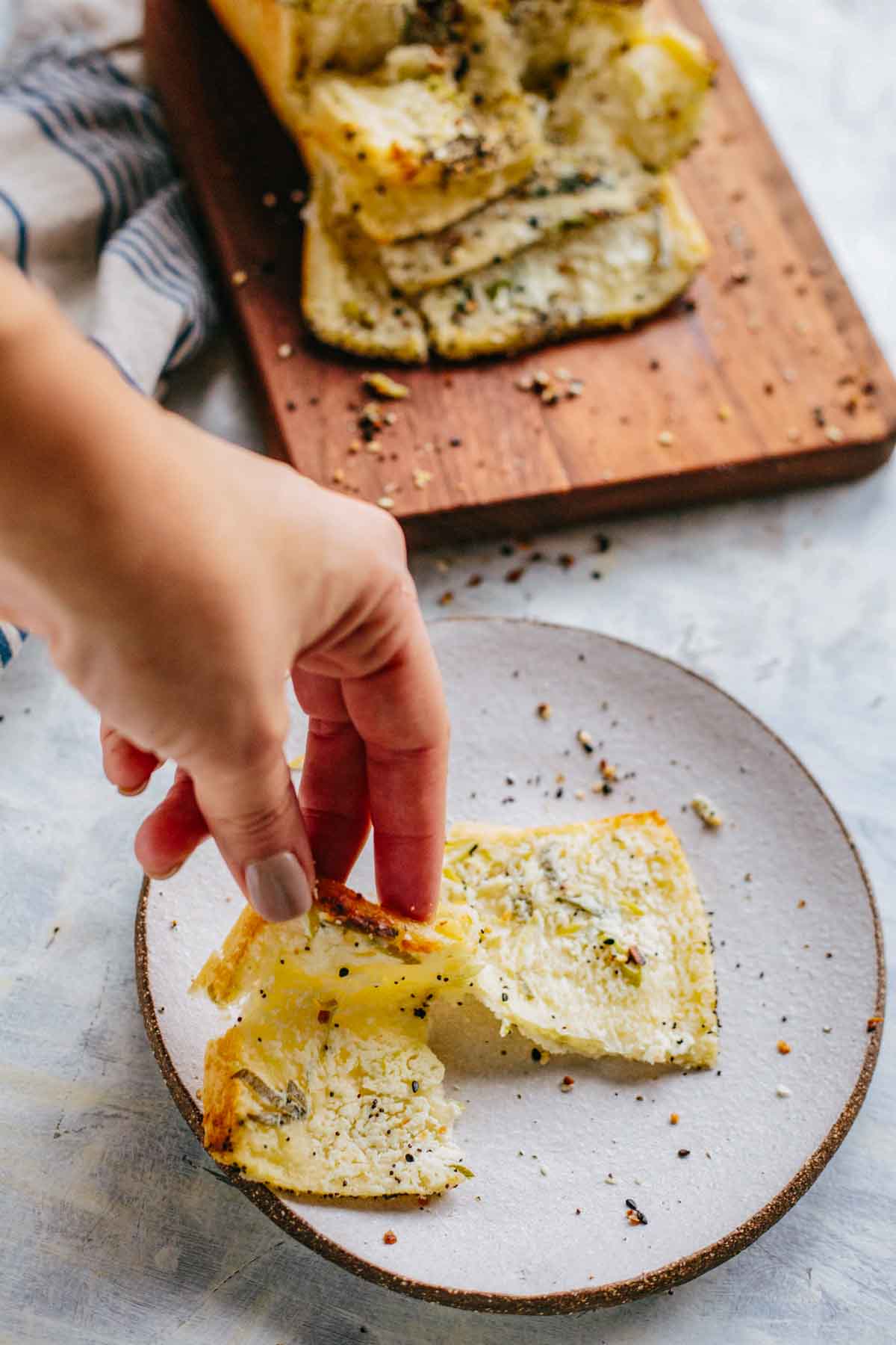 Hand lifting a soft, cheesy slice from a plate, showing texture and seasoning.