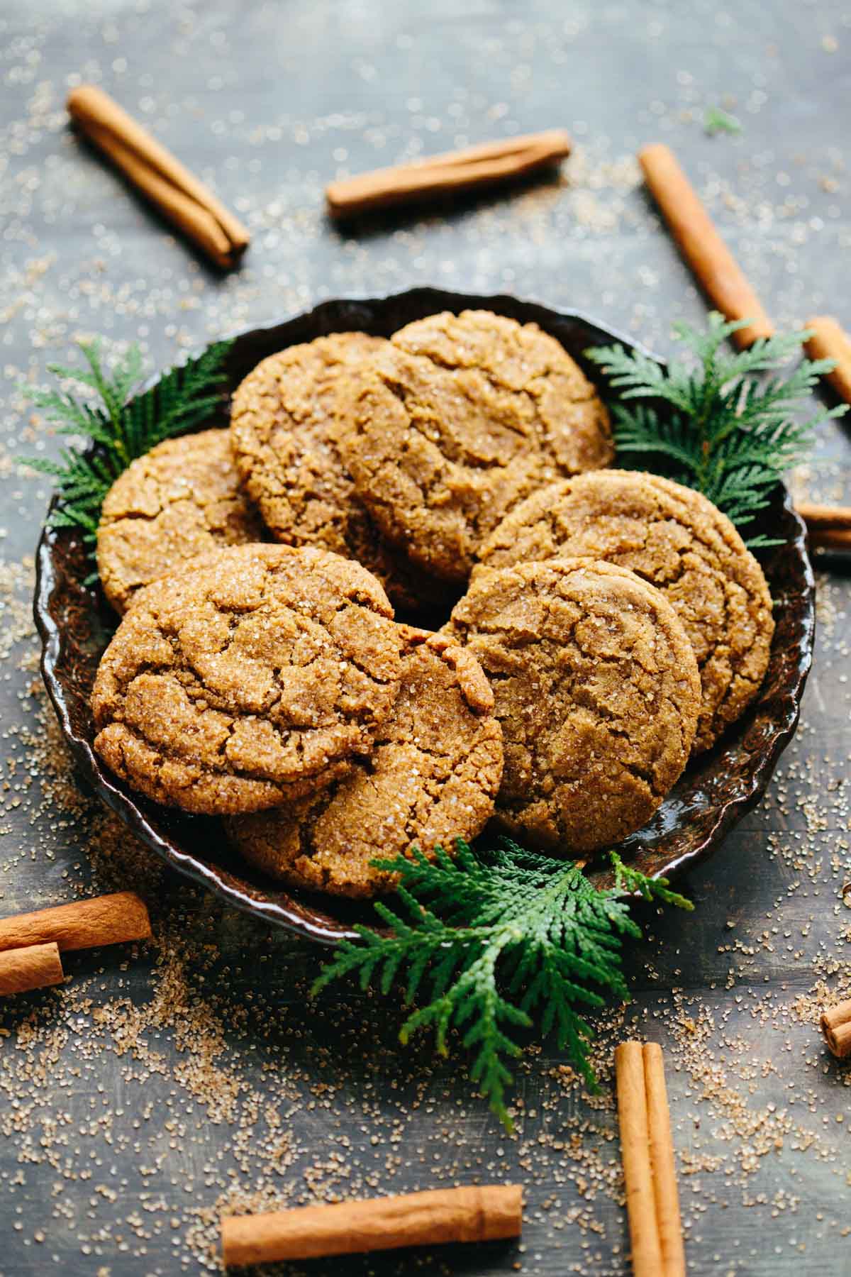 Overhead view of a plate filled with ginger molasses cookies and scattered cinnamon sticks for a cozy holiday feel.