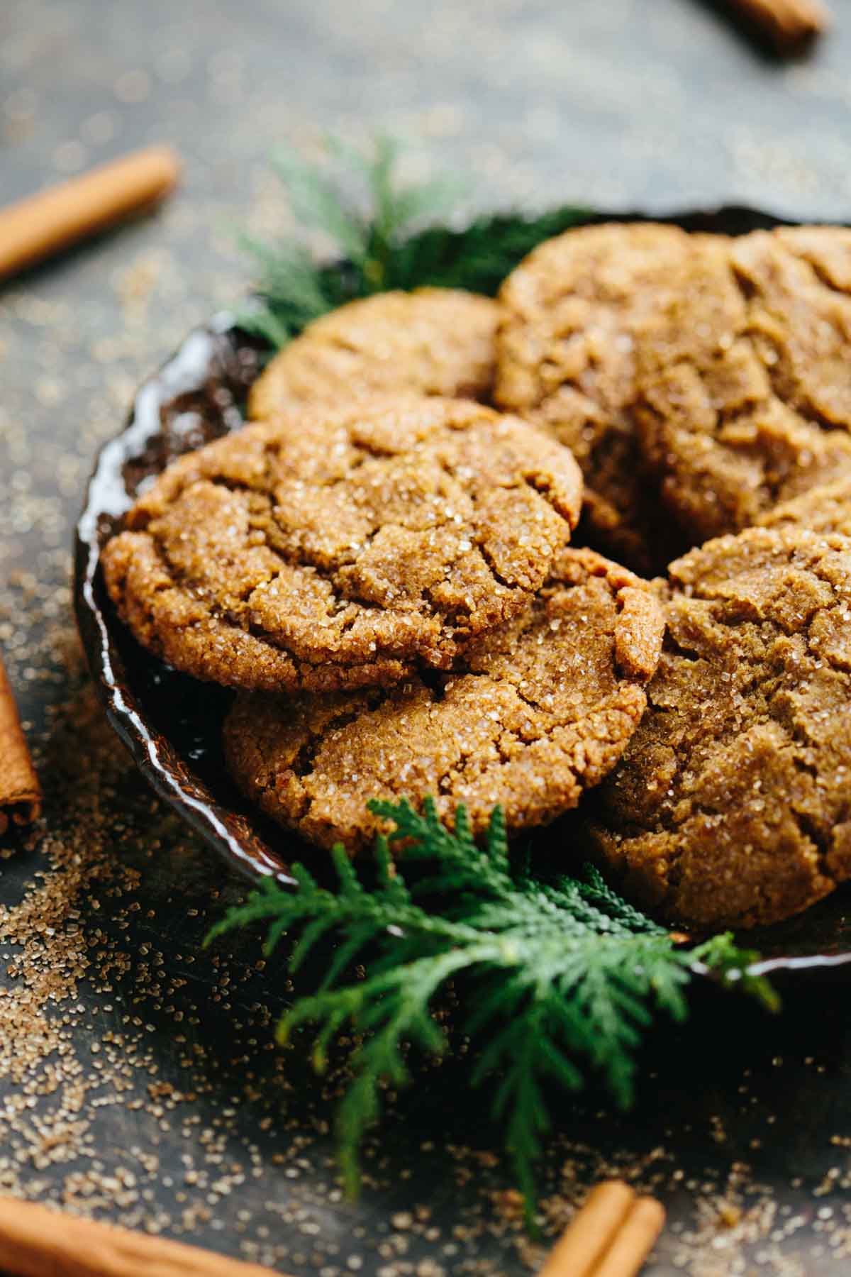 Close-up of sugar-coated ginger molasses cookies stacked on a rustic plate with greenery accents.