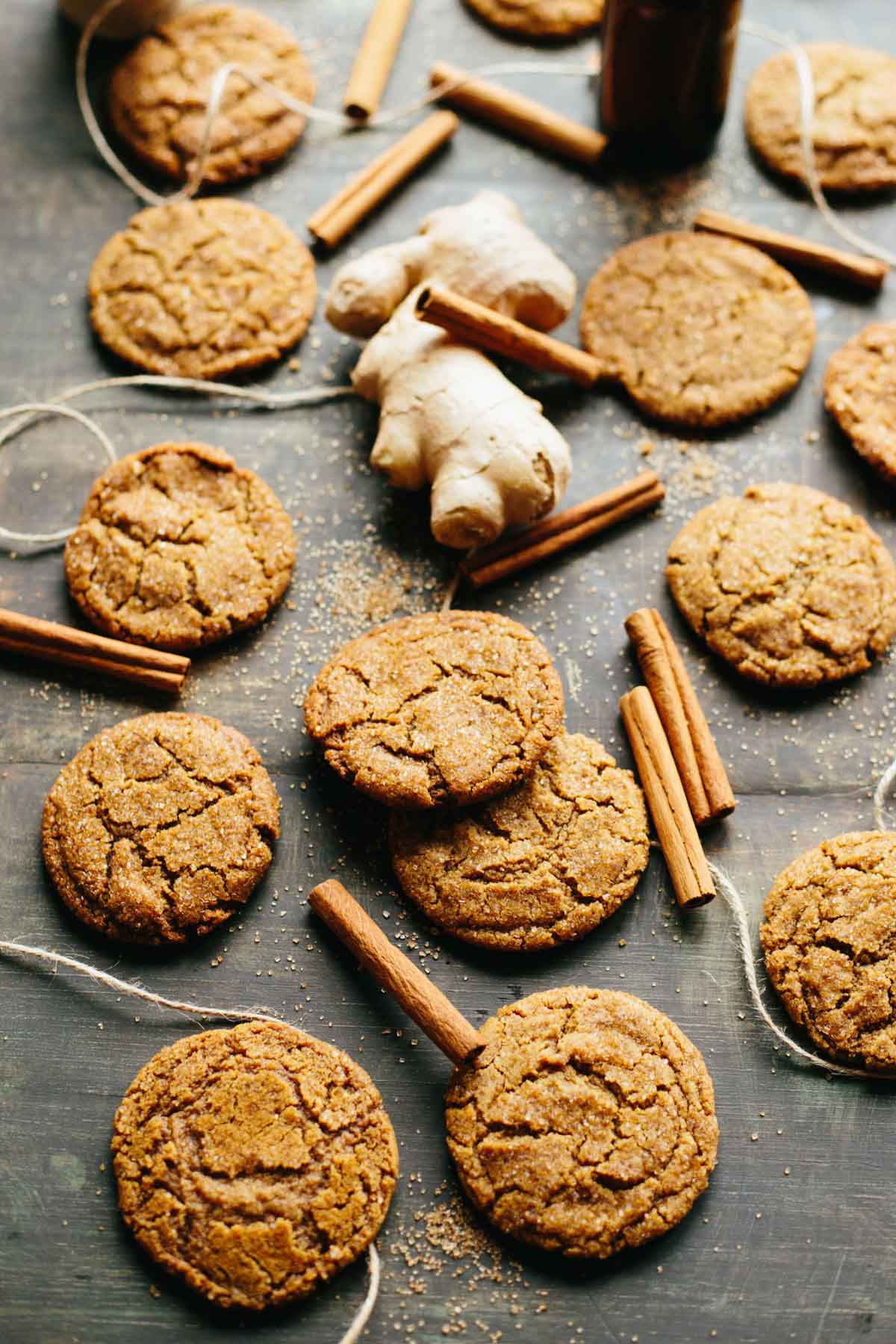 Overhead view of multiple ginger molasses cookies laid out on a baking surface with cinnamon sticks and ginger root.