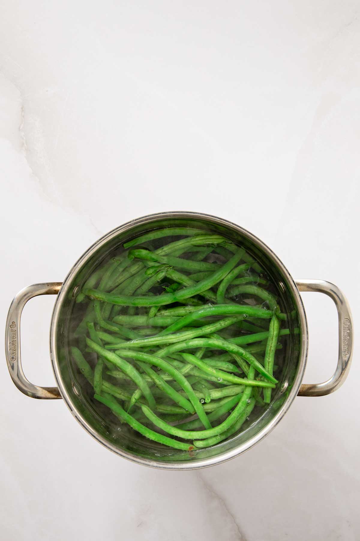 Fresh green beans blanching in a large stainless steel pot of boiling water.