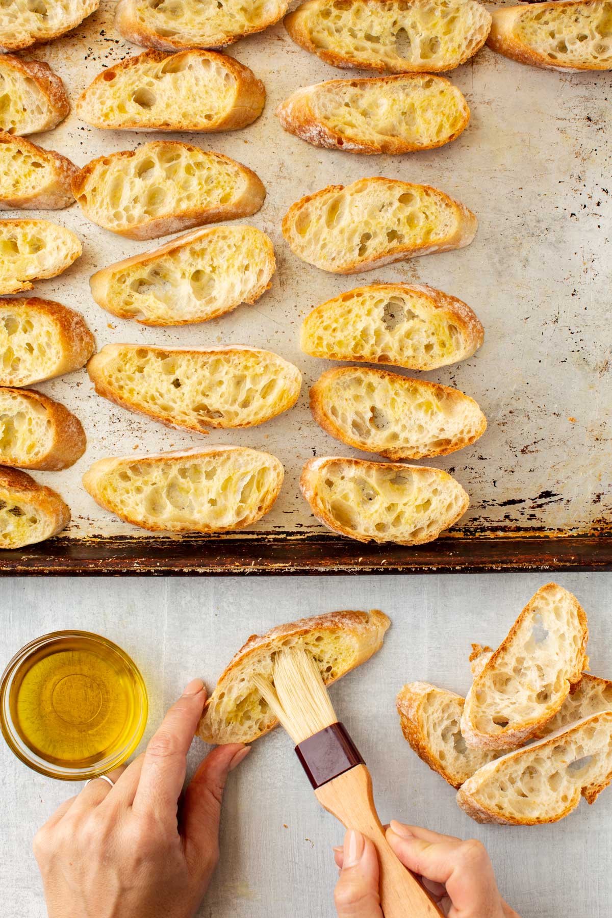 Brushing sliced baguette pieces with olive oil using a pastry brush before baking.