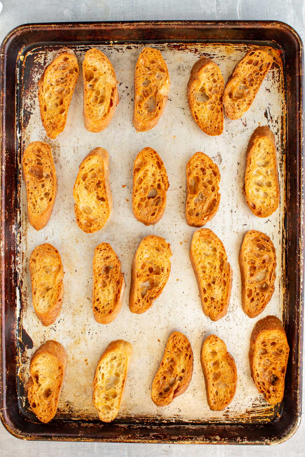 Golden brown crostini just out of the oven on a well-used baking sheet, showing crisp texture and even color.
