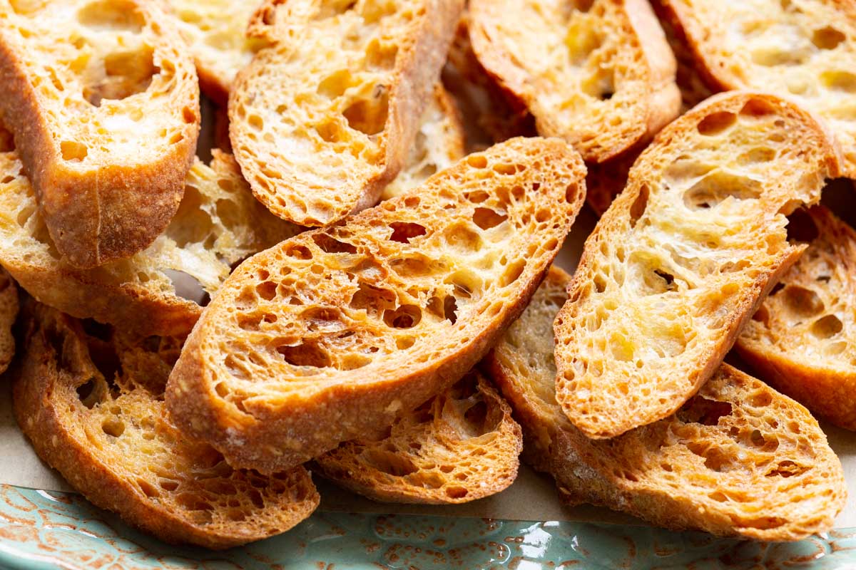 Close-up of crispy toasted crostini piled on a platter, highlighting the airy crumb and golden crust.