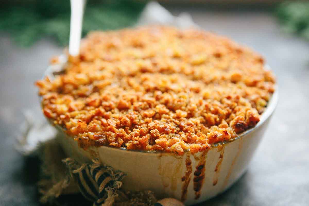Side view of a bubbling kale gratin with browned, crunchy breadcrumbs spilling slightly over the edge of the dish.