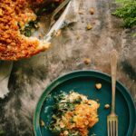 Overhead shot of a kale gratin with a slice removed, revealing creamy greens beneath the crunchy golden topping, served next to a plated portion with a fork.