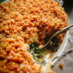 Close-up of a spoonful taken from the kale gratin, highlighting the creamy sauce and layers of wilted kale under the browned breadcrumb crust.