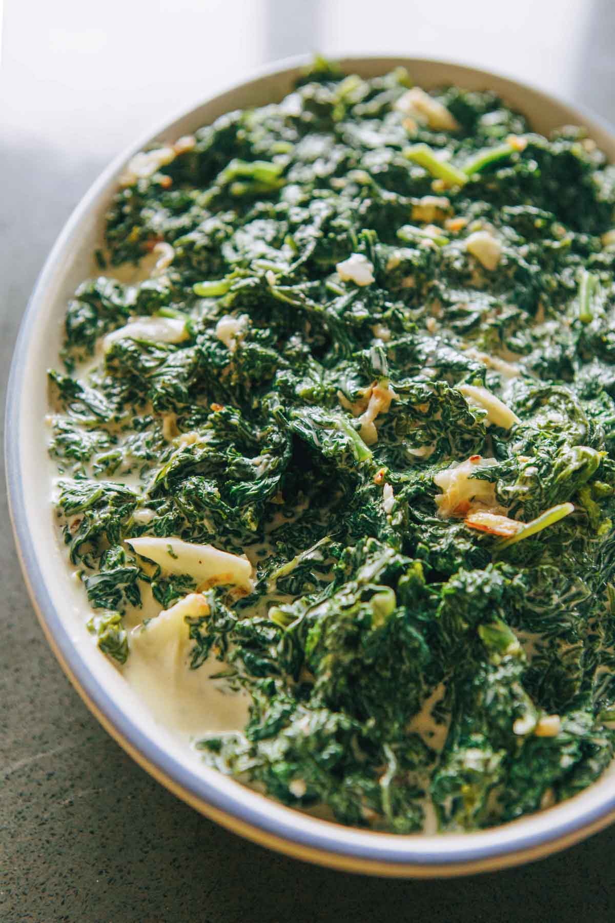 Unbaked kale gratin in a baking dish filled with creamy kale mixture before being topped and baked, showing bright green greens coated in sauce.